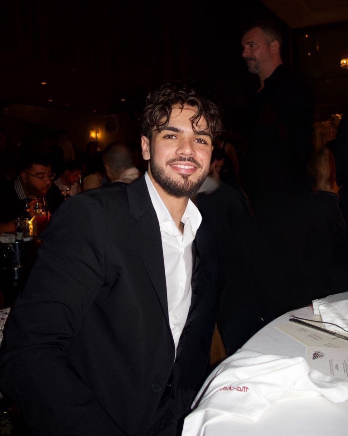 Nicolò in a dark suit, seated at a dinner table